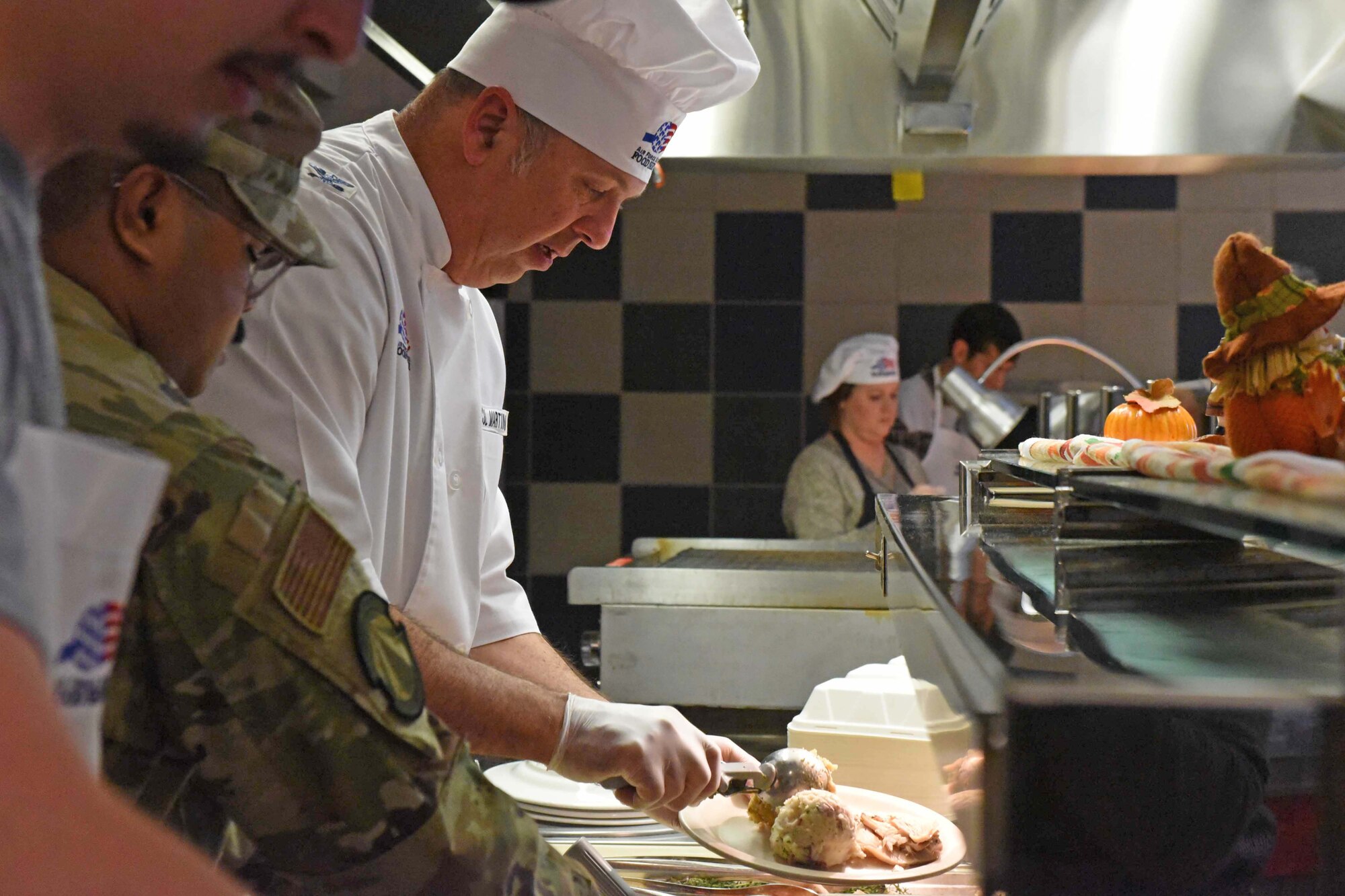 Airmen in chefs coat serve meals in cafeteria line
