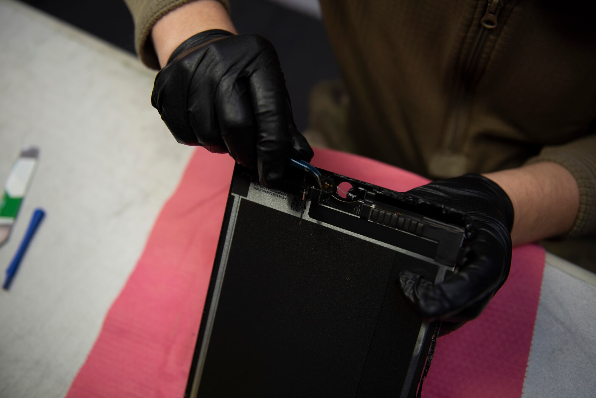A photo of an Airman removing a home button from a tablet