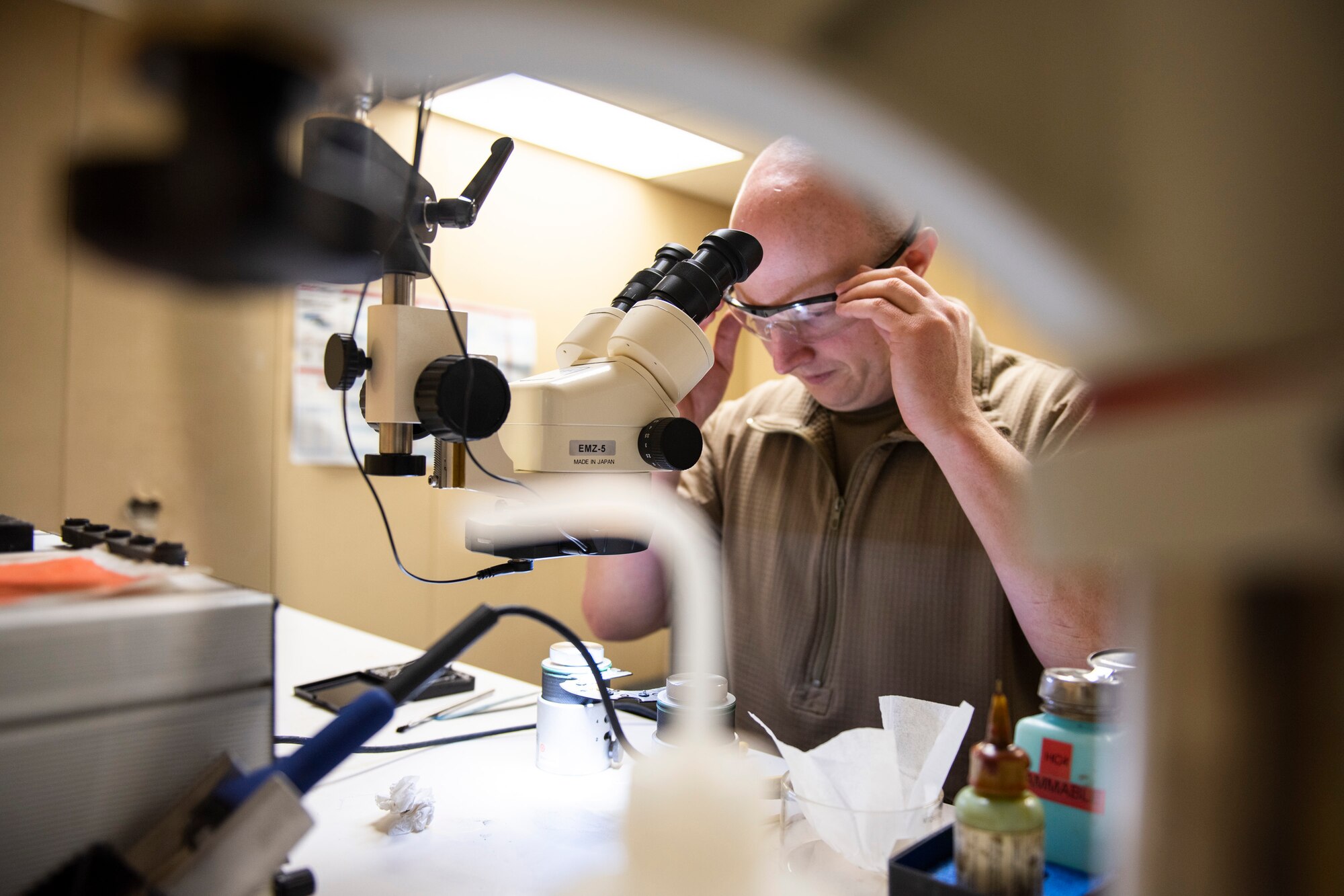 A photo of an Airman putting on a pair of safety goggles before repairing electronic equipment