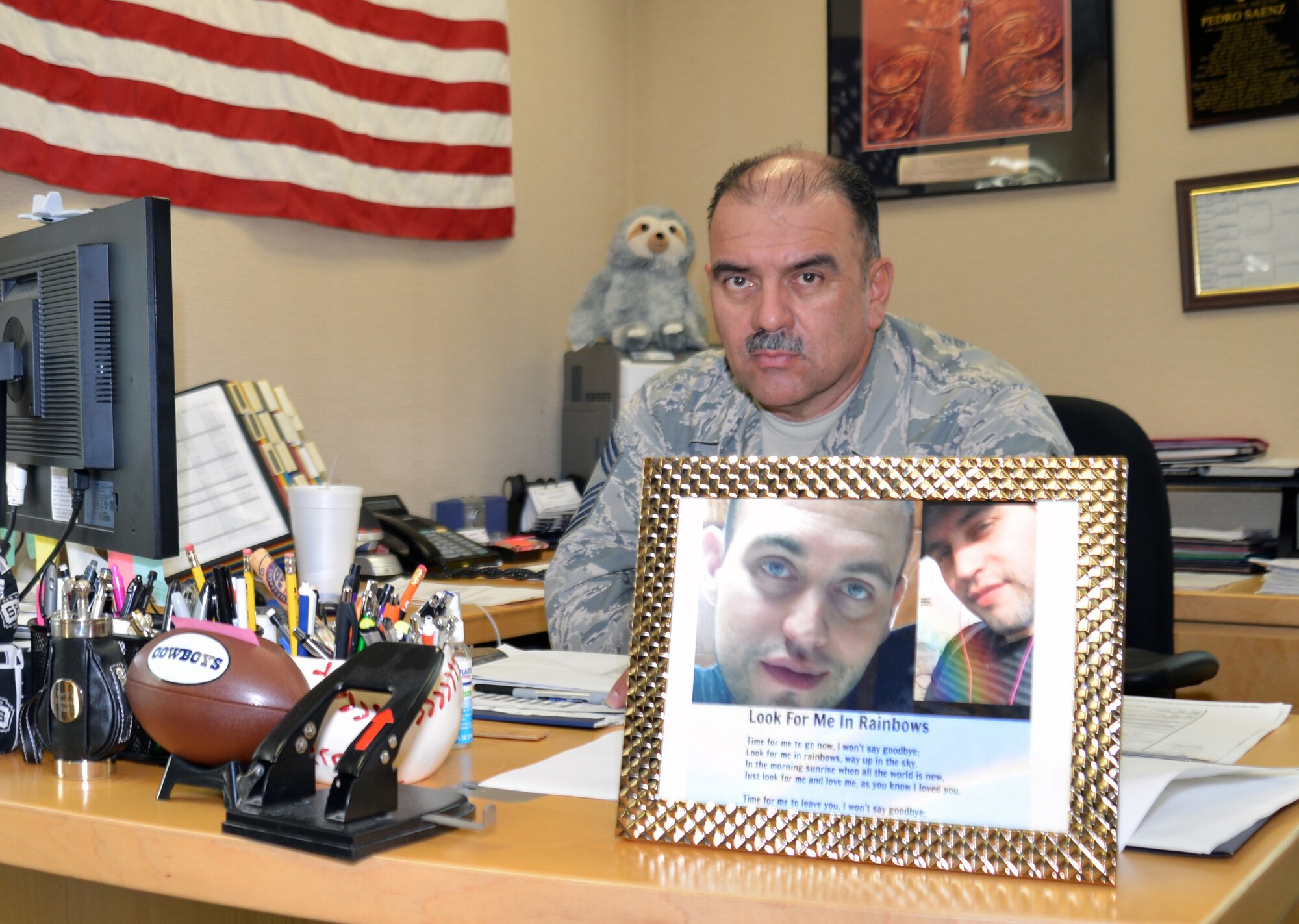 Chief Master Sgt. Pedro Saenz, a 433rd Aircraft Maintenance superintendent, sits at the desk in his office with his son’s photo in the foreground and his son’s favorite stuffed animal, the sloth in the background.