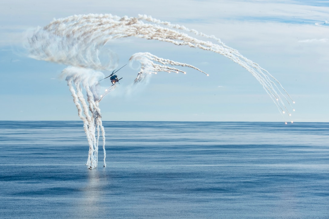 A helicopter fires flares while flying over the ocean.