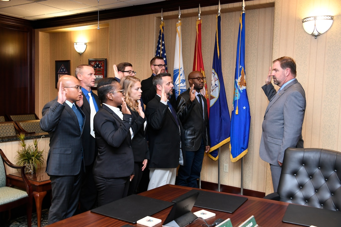 Eight new associates stand in front of flags with their right hand raised