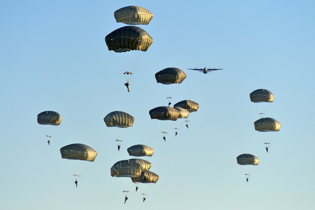 A group of soldiers with green parachutes descend in the sky after exiting an aircraft.