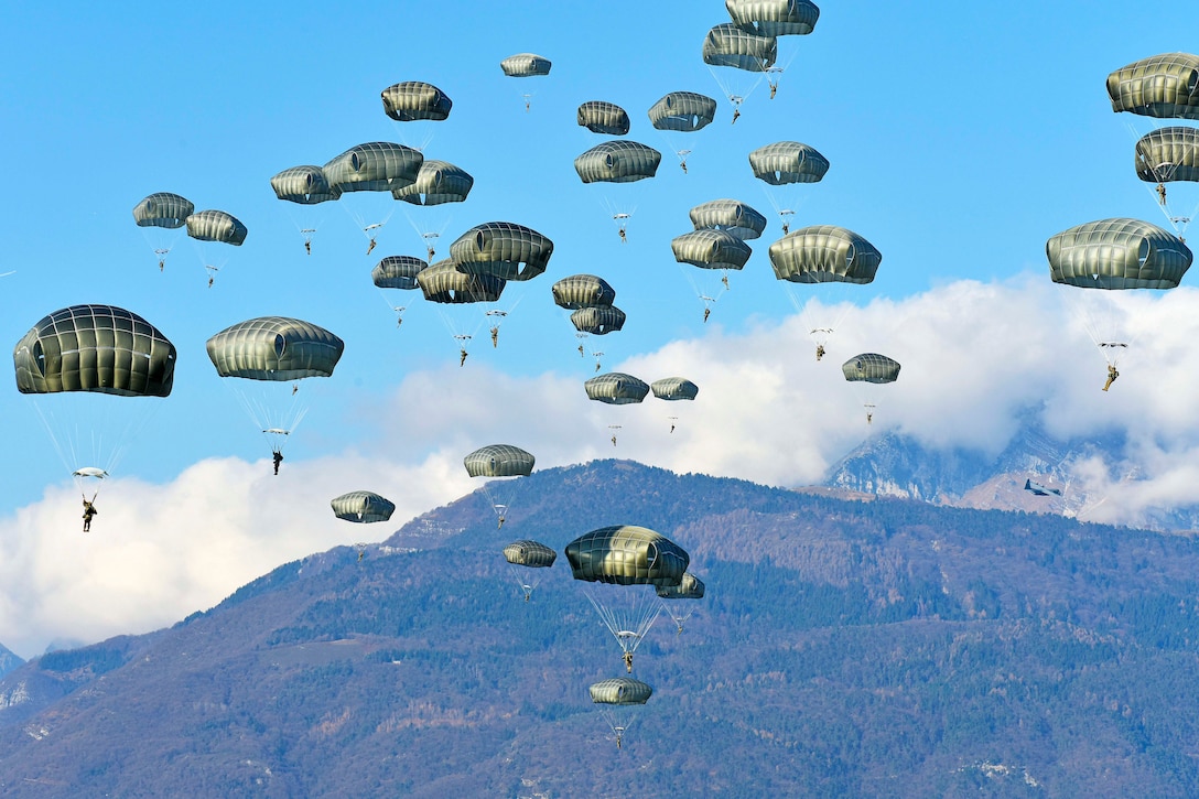 Soldiers descend through the sky wearing parachutes.