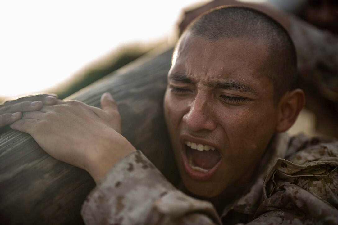 A Marine holds a log on his shoulder.