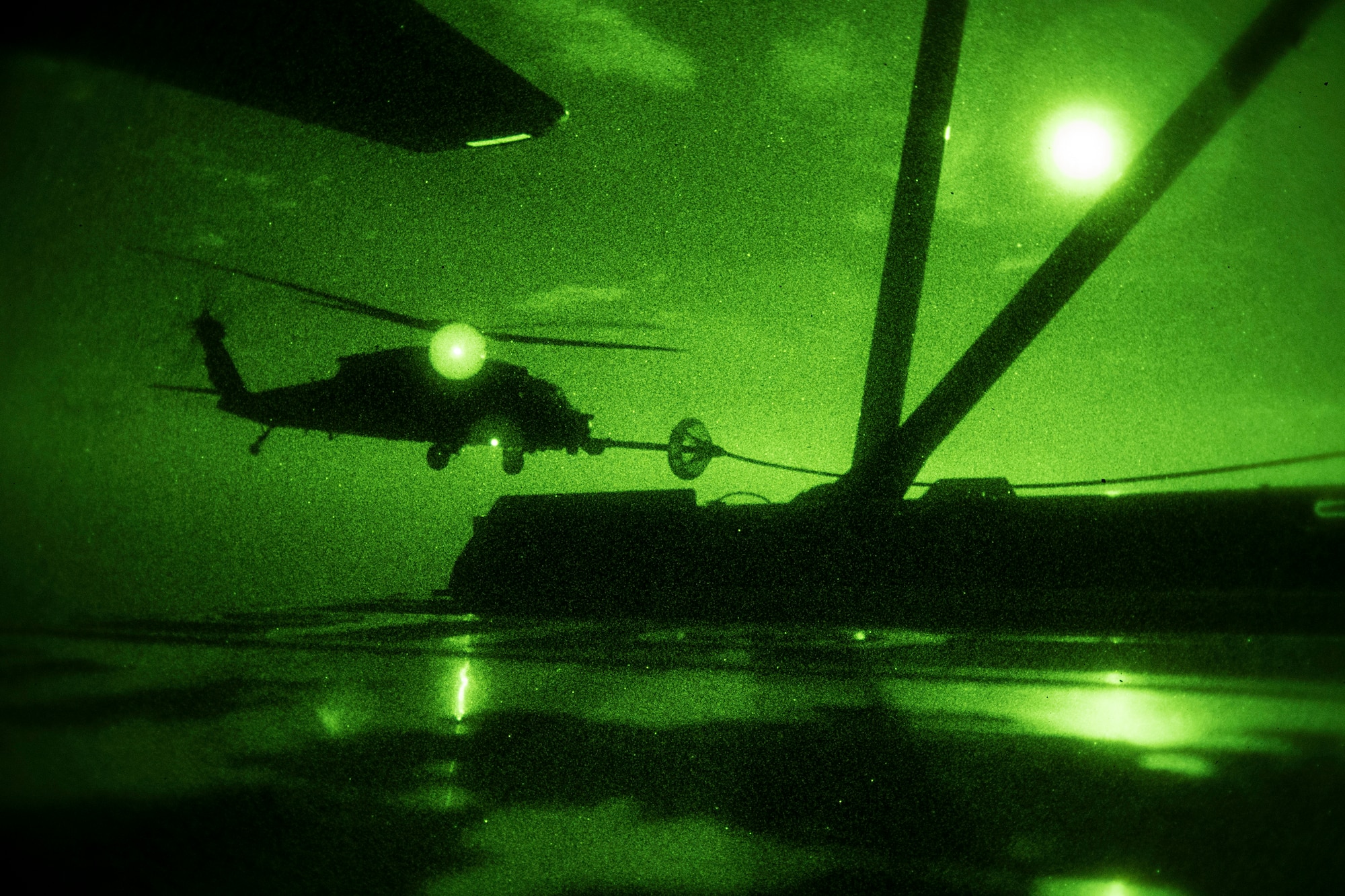 A night vision photo of a military rescue helicopter receiving fuel from a carrier aircraft.