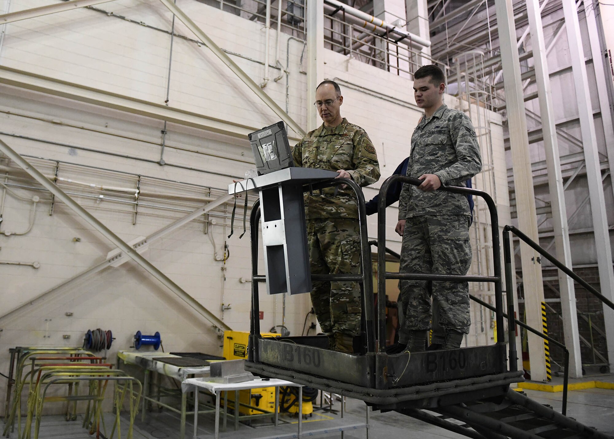 Two Airmen look at a metal stand used to hold tools and a laptop.