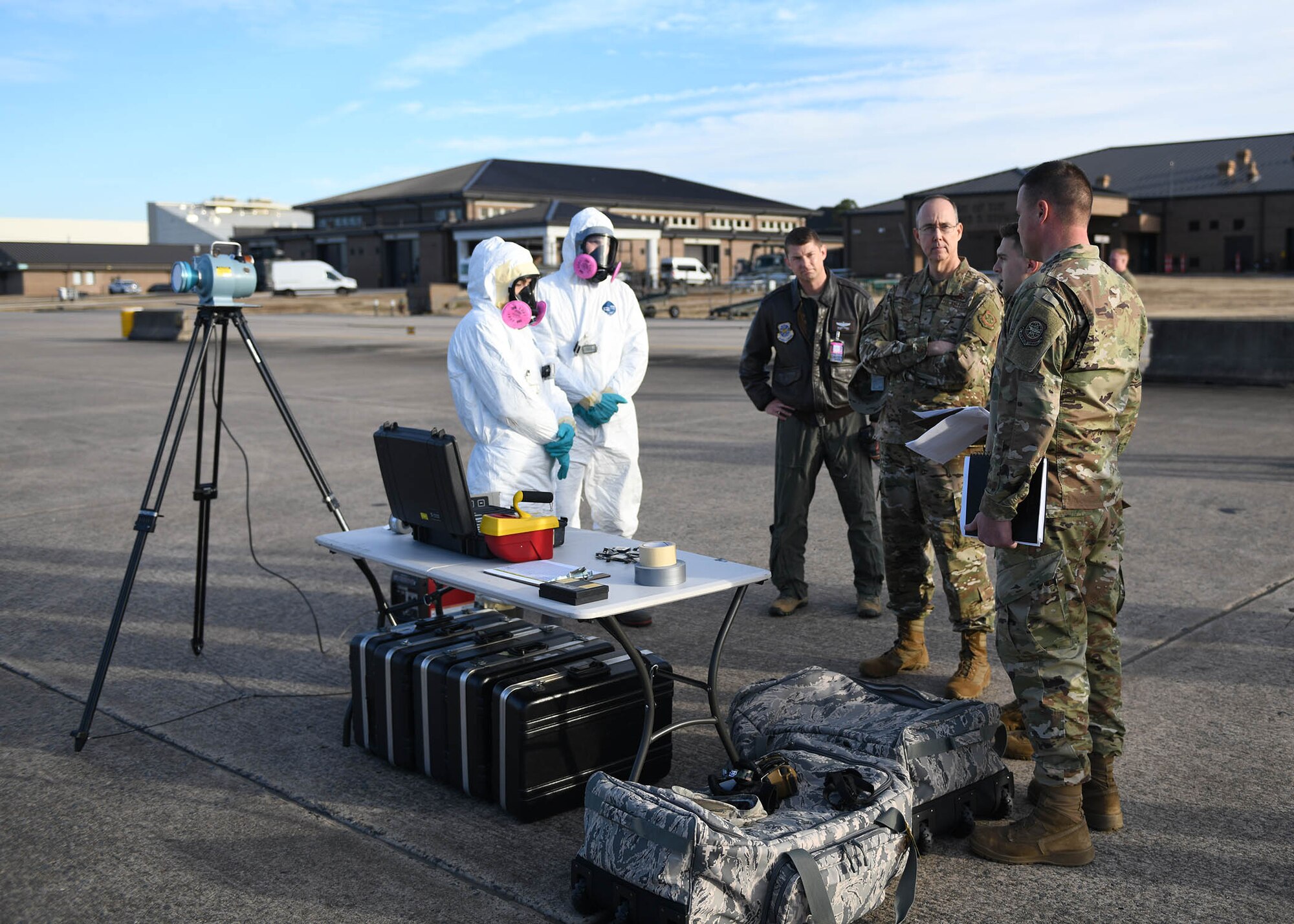 Three Airmen inspect Airmen who are wearing chemical gear.