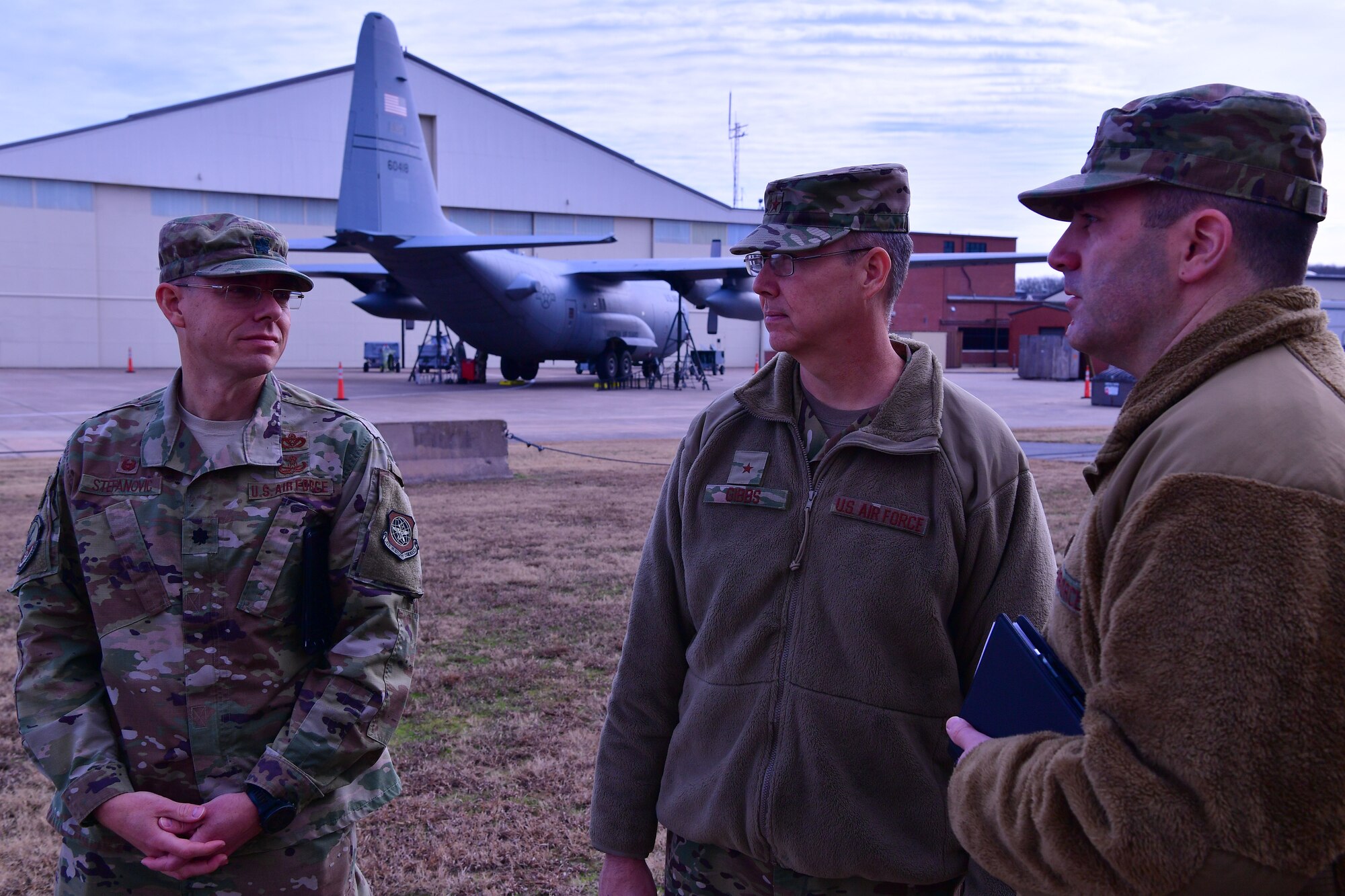 3 Airmen stand with a C-130J Super Hercules behind them.