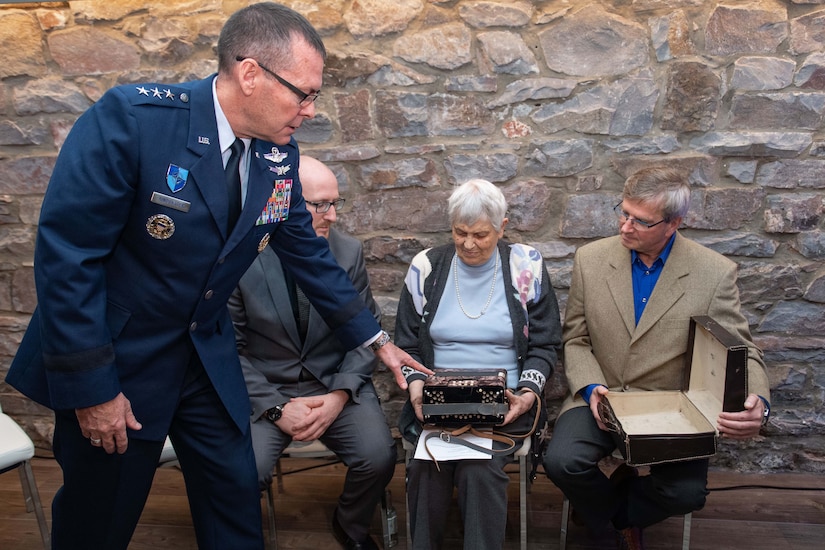 General points to accordion as two men and a woman inspect it.