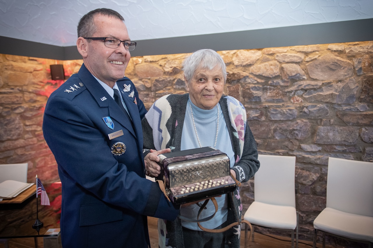 Air Force three-star general presents accordion to woman.