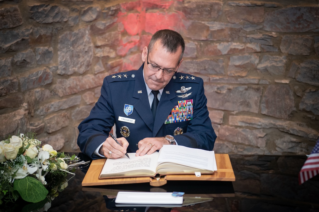 Air Force three-star general signs a book while seated at a table.