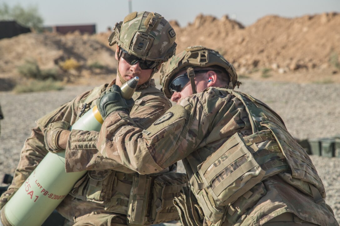 Two soldiers handle an artillery shell.