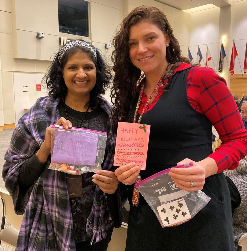 Yasmin Dossa, a DLA Troop Support Industrial Hardware integrated support team supervisor, left, and Megan Ward, a Troop Support IH purchasing agent, pose with cards to be sent along with morale and resilience bags to deployed warfighters December 3, 2019, in Philadelphia.