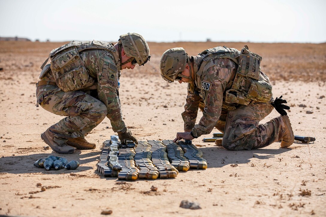 Two soldiers align ammunition on the ground.