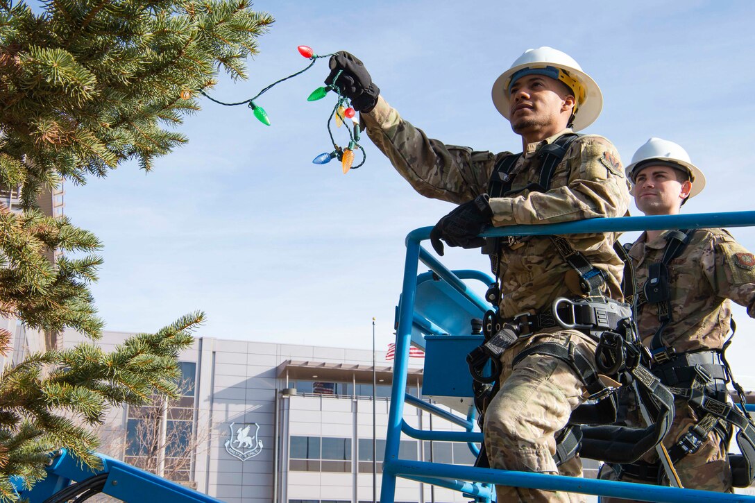Two airmen put Christmas lights on a tree.