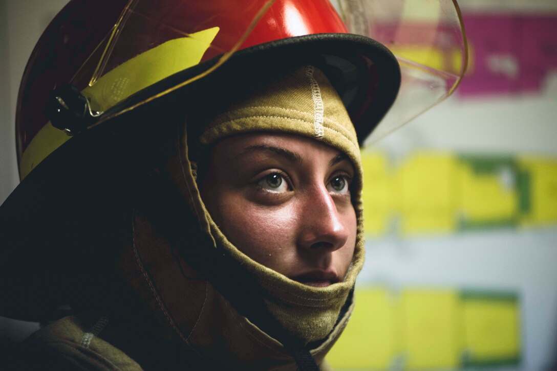 A Coast Guardsman wearing a firefighting helmet looks at something aboard a ship.