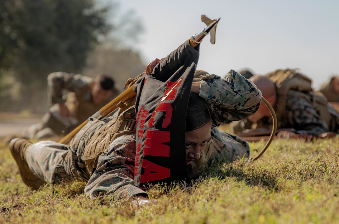 Sgt. Lynarae Pena, a tactical switching operator with Reserve Base Support, Marine Forces Reserve, low crawls to the objective while carrying the guidon during Martial Arts Instructor Course 1-20 aboard Naval Air Station Joint Reserve Base New Orleans, Dec. 4, 2019. The course consists of both physical and mental challenges to mold Martial Arts Instructors.
