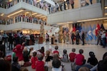 Santa Claus walks down stairs as HQC CDC children wave and HQC employees look on during the HQC annual tree lighting ceremony.