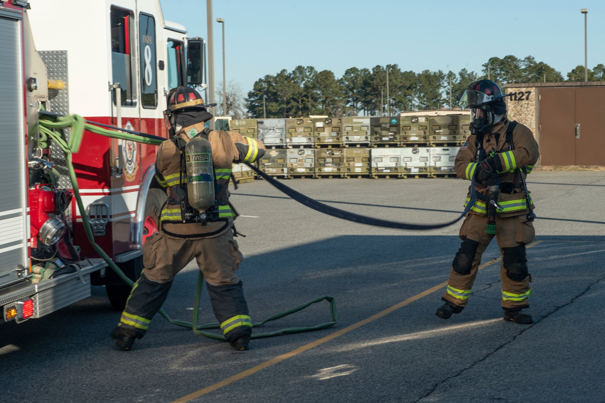 A photo of Airmen removing a hose from a fire truck during an evacuation drill.