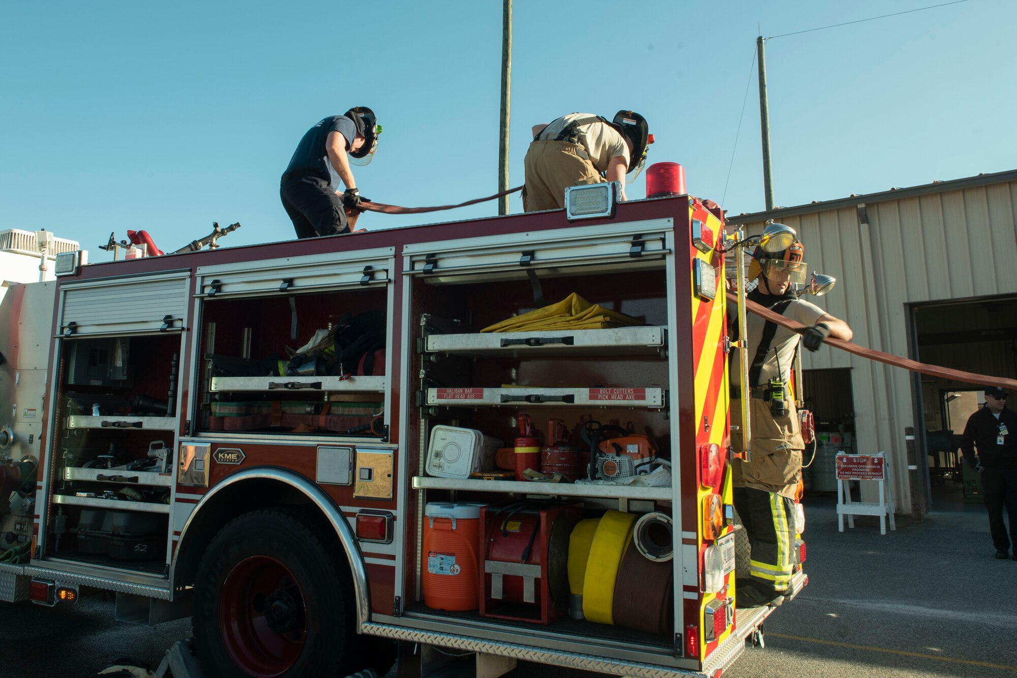 Photo of three Airmen packing up a firetruck after an evacuation drill.