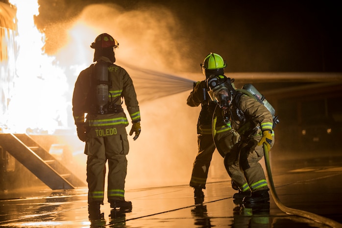 U.S. Marines with Aircraft Rescue and Firefighting, Headquarters and Headquarters Squadron, Marine Corps Air Station Yuma conduct low light hand line drills during live burn training on MCAS Yuma, Ariz., Nov. 21, 2019. Hand line drills focus on techniques to push fuel fires away from aircraft, ARFF Marines train monthly to enhance their readiness when responding to emergencies on the flight line.