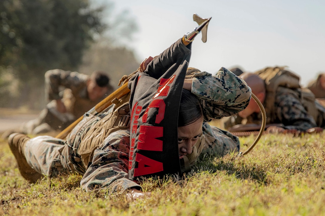 A Marine crawls on the ground while carrying a guidon.