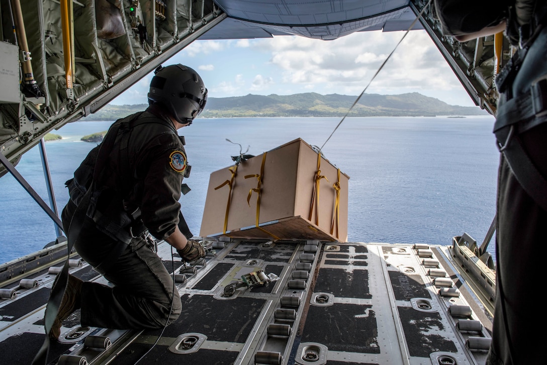 An airman drops a box from the back of an open aircraft.