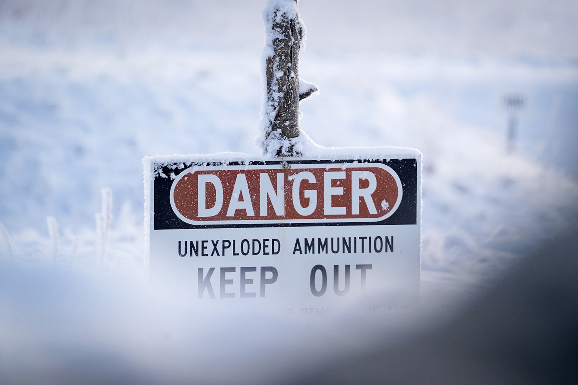 A sign warning of unexploded ammunition is seen covered in hoar frost as paratroopers assigned to the 2nd Battalion, 377th Parachute Field Artillery Regiment, 4th Infantry Brigade Combat Team (Airborne), 25th Infantry Division, U.S. Army Alaska, use M240B, and M2 machine guns while conducting live-fire qualification at Grezelka range, on Joint Base Elmendorf-Richardson, Alaska, Dec. 5, 2019. The Soldiers practiced identifying, and engaging targets at varying distances to solidify their proficiency with the weapons in sub-arctic conditions.