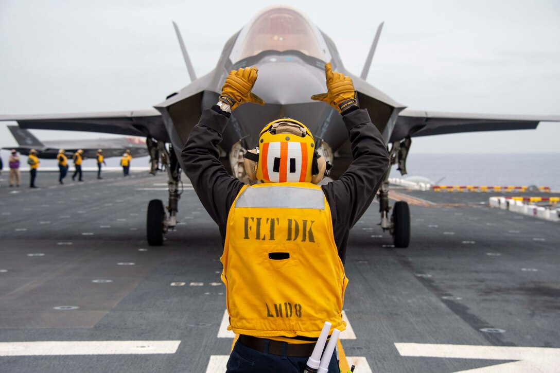 A sailor holds up his hands toward a plane.