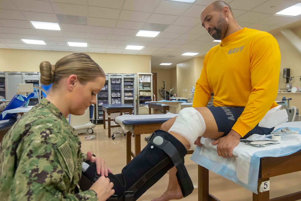 A sailor puts a medical boot on another sailor.