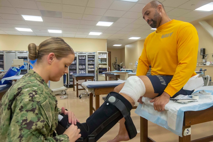 A sailor puts a medical boot on another sailor.