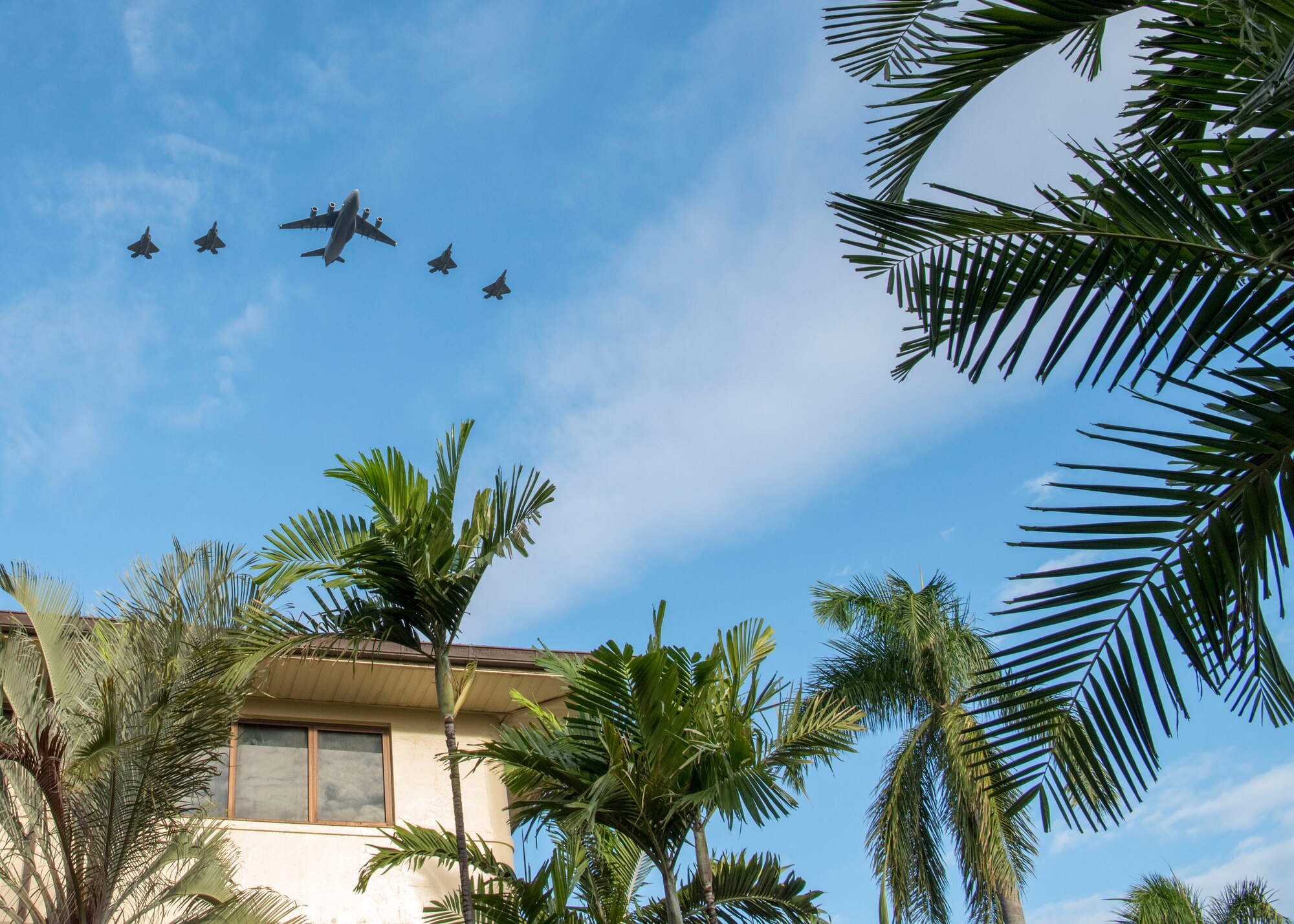 A C-17 Globemaster and four F-22 Raptors conduct a flyover over the Pacific Air Forces Headquarters on Joint Base Pearl Harbor-Hickam, Hawaii, Dec. 5, 2019.