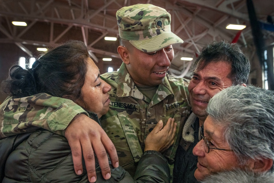 A soldier puts his arms around a smiling man and woman as another woman stands by.