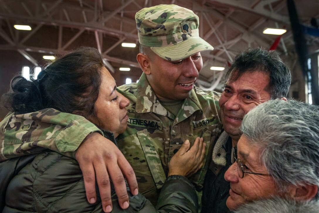 A soldier puts his arms around a smiling man and woman as another woman stands by.