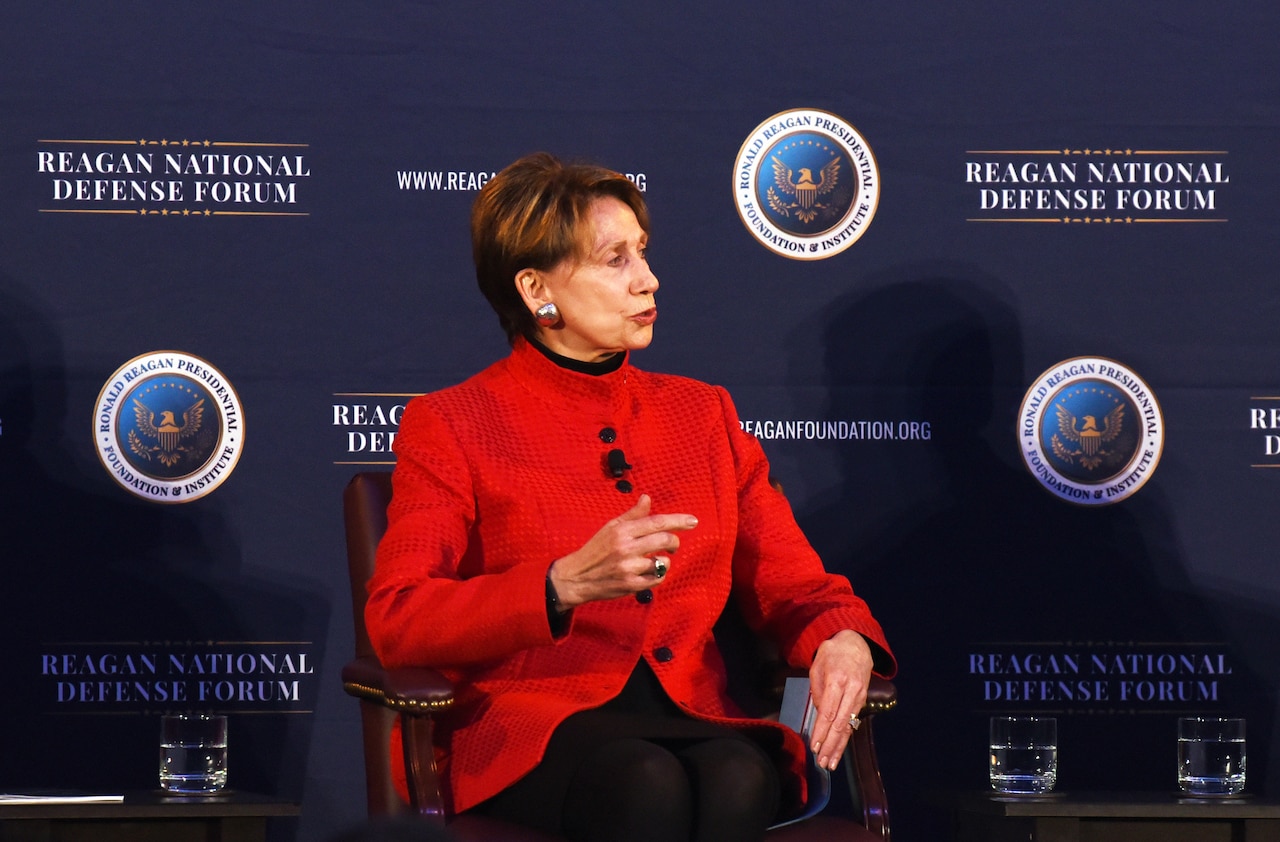 A woman sits in a chair on stage. A backdrop reads "Reagan National Defense Forum."
