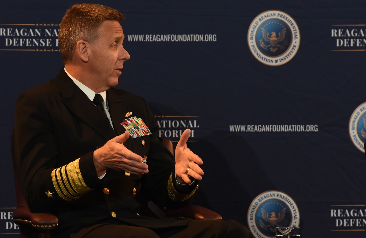 Navy admiral in uniform gestures while speaking.
