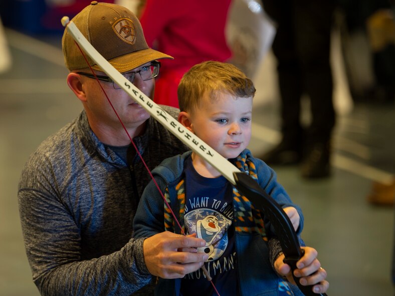 Lt. Col. Bryan Dutcher, U.S. Space Command deputy battle watch commander, and his son, Davis, 3, participate in the safe archery booth at the annual Children’s Holiday Fest, Dec. 7, 2019, at Schriever Air Force Base, Colorado. The booth allowed families to practice archery safely by firing at floating rubber balls during the event. (U.S. Air Force photo by Airman 1st Class Jonathan Whitely)