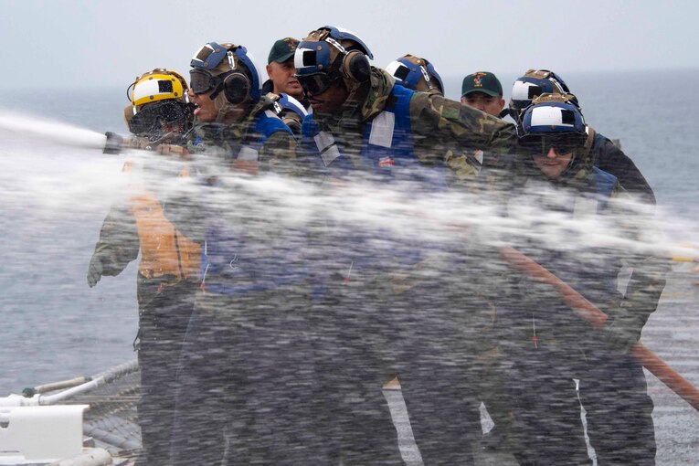A group of sailors use a water hose.