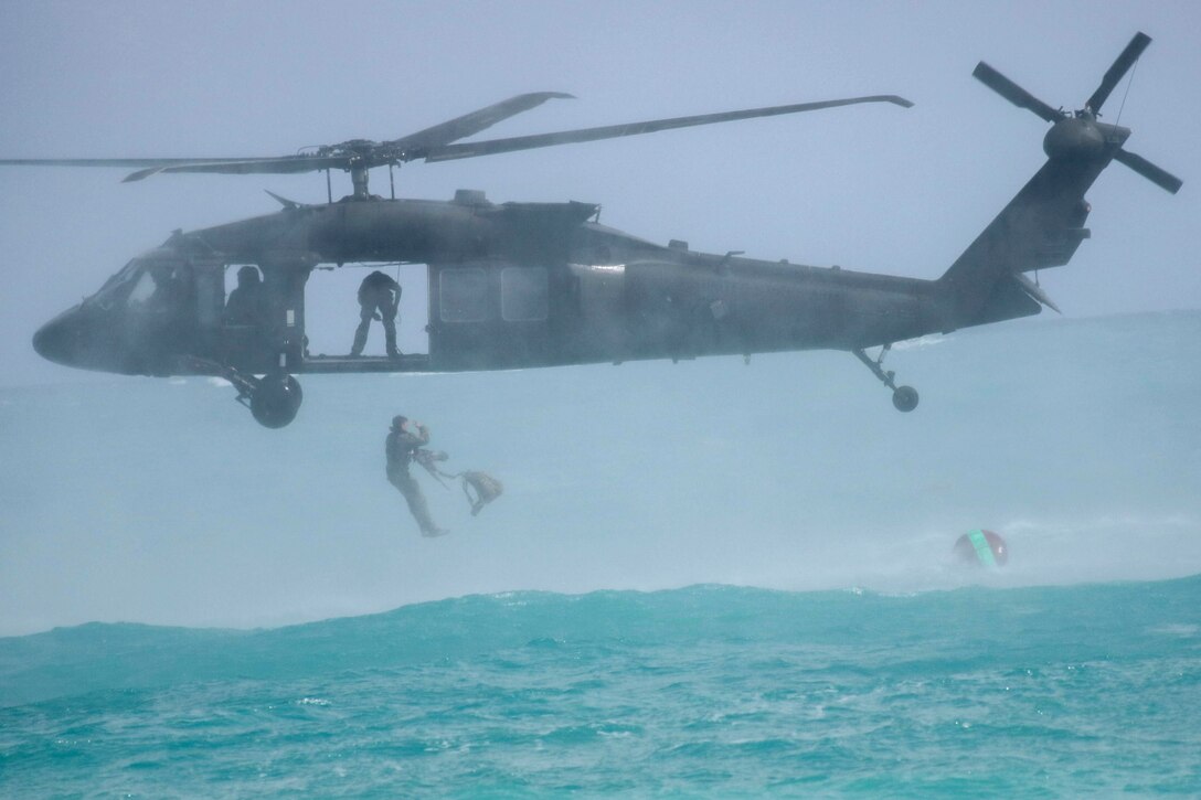 Soldiers jump from a helicopter into water.