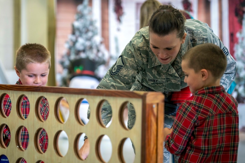 An airman talks with two children by a large wooden upright game board.