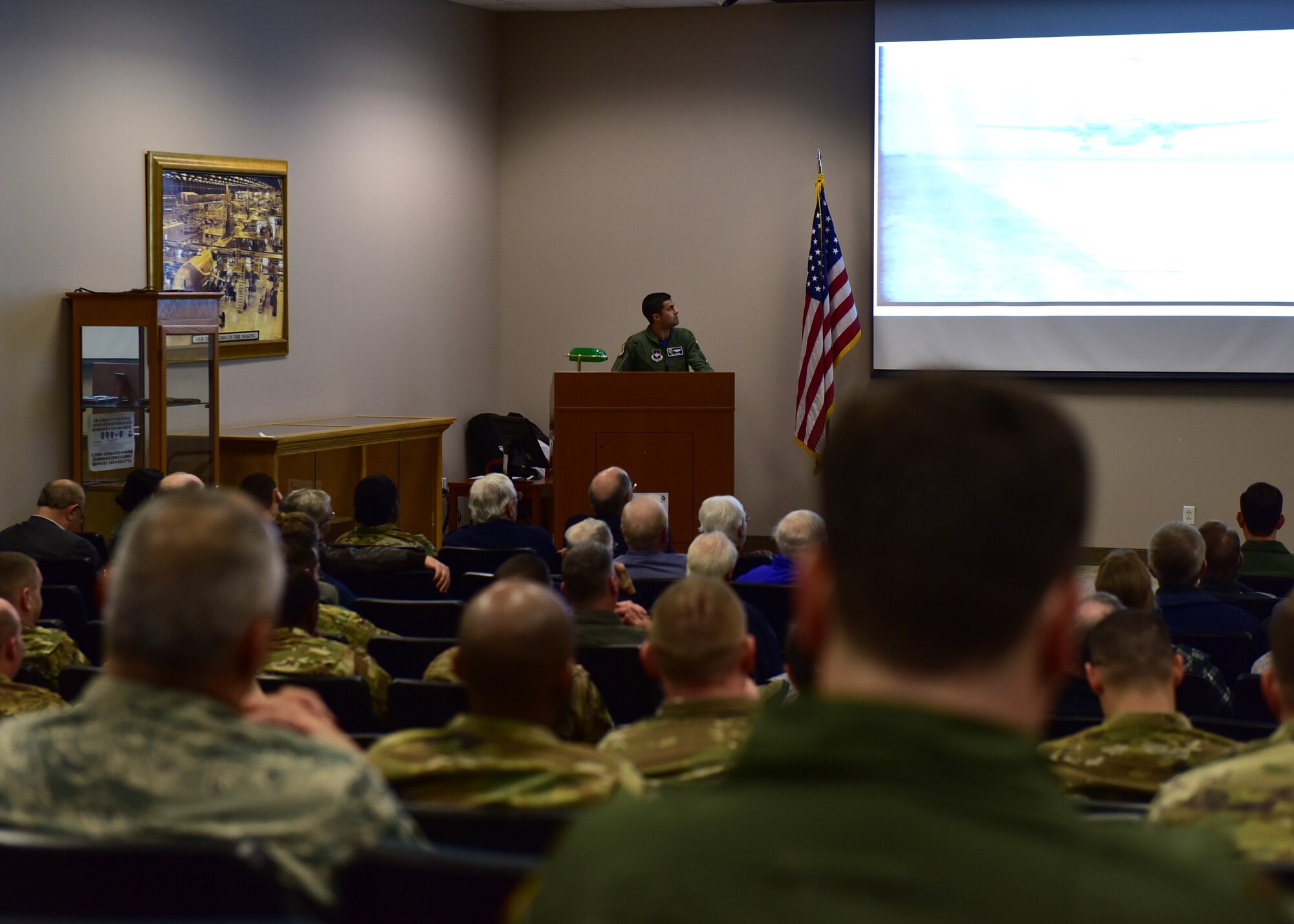 Individuals gather in a building, some in uniform, for a reunion, listening to speakers and observing dedications.