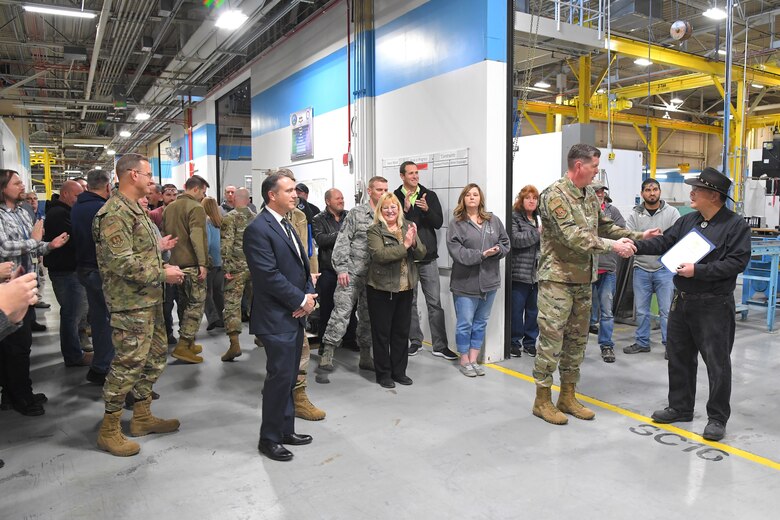 Lt. Gen. Gene Kirkland shakes hands with employee Matthew Yun, 581st Missile Maintenance Squadron, to recognize him for 40 years of federal service in the bay of maintenance warehouse while several other employees and guests watch the presentation.