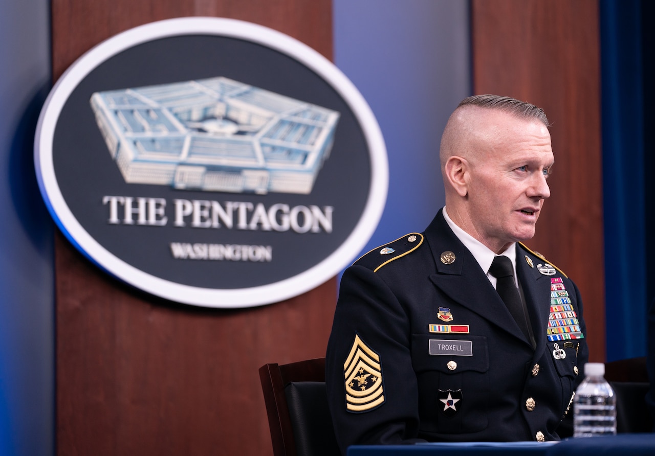 A uniformed service member sits behind a table and speaks into a microphone. Behind him, a sign on the wall reads “The Pentagon - WASHINGTON.”