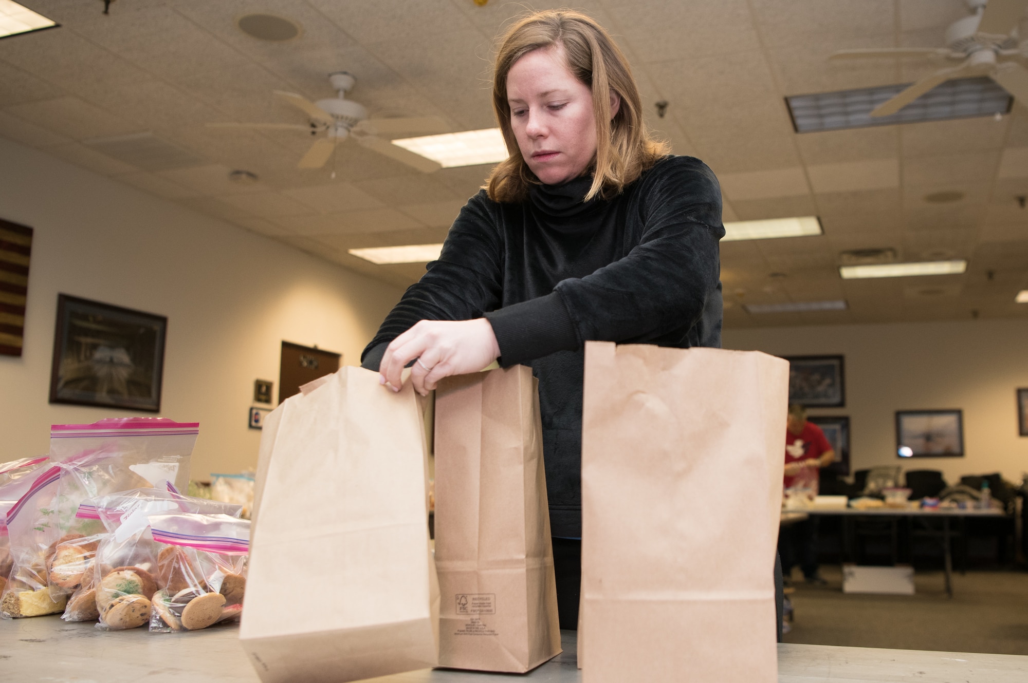 Lacey Szczepanik fills paper bags with cookies and baked goods during Operation Cookie Drop Dec. 9, 2019, at the 9th Airlift Squadron on Dover Air Force Base, Del. The Dover Spouses’ Club volunteers its time to bake or package cookies and other baked goods. (U.S. Air Force photo by Mauricio Campino)