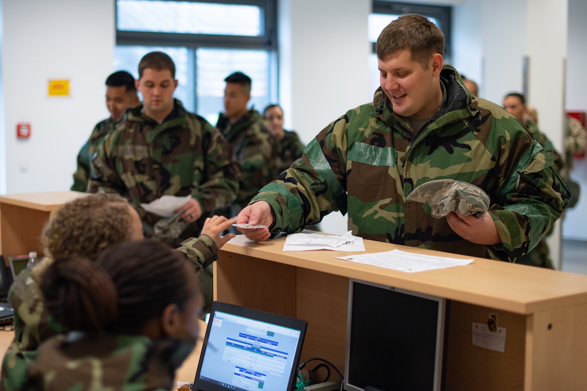 U.S. Air Force Senior Airman Jared Sivec, 86th Aerospace Medical Squadron bioenvironmental engineering technician, hands his ID to military personnel section Airmen during exercise Operation Varsity 19-04 at the Individual Deployment Readiness Center, Ramstein Air Base, Germany, Dec. 9, 2019. The MPS implemented a mass in-processing line to efficiently provide large groups of Airmen with the information they need to process into Ramstein. (U.S. Air Force photo by Staff Sgt. Devin Boyer)