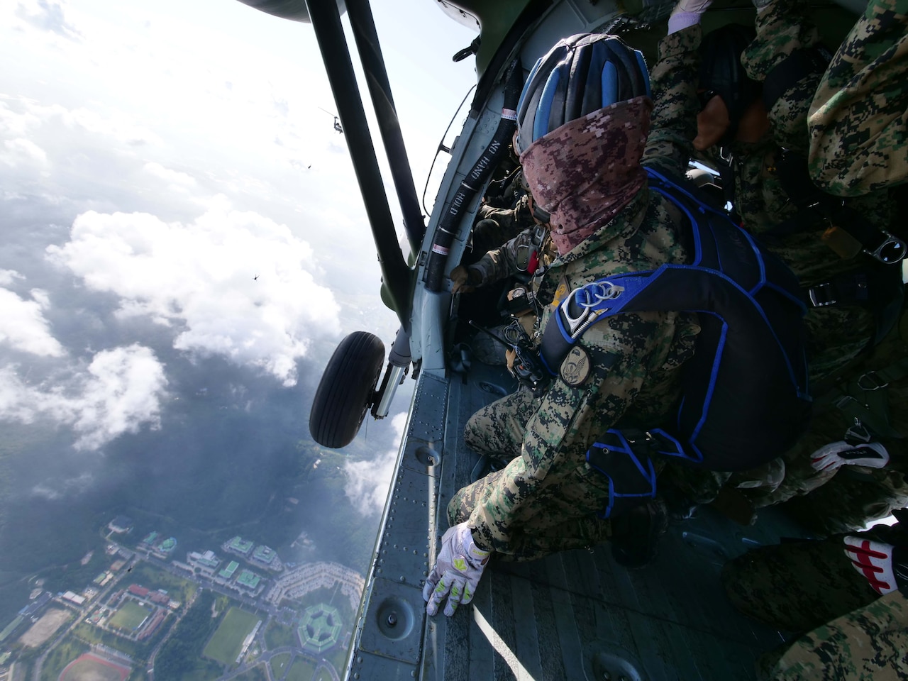 Person looks at parachutists from inside a helicopter.