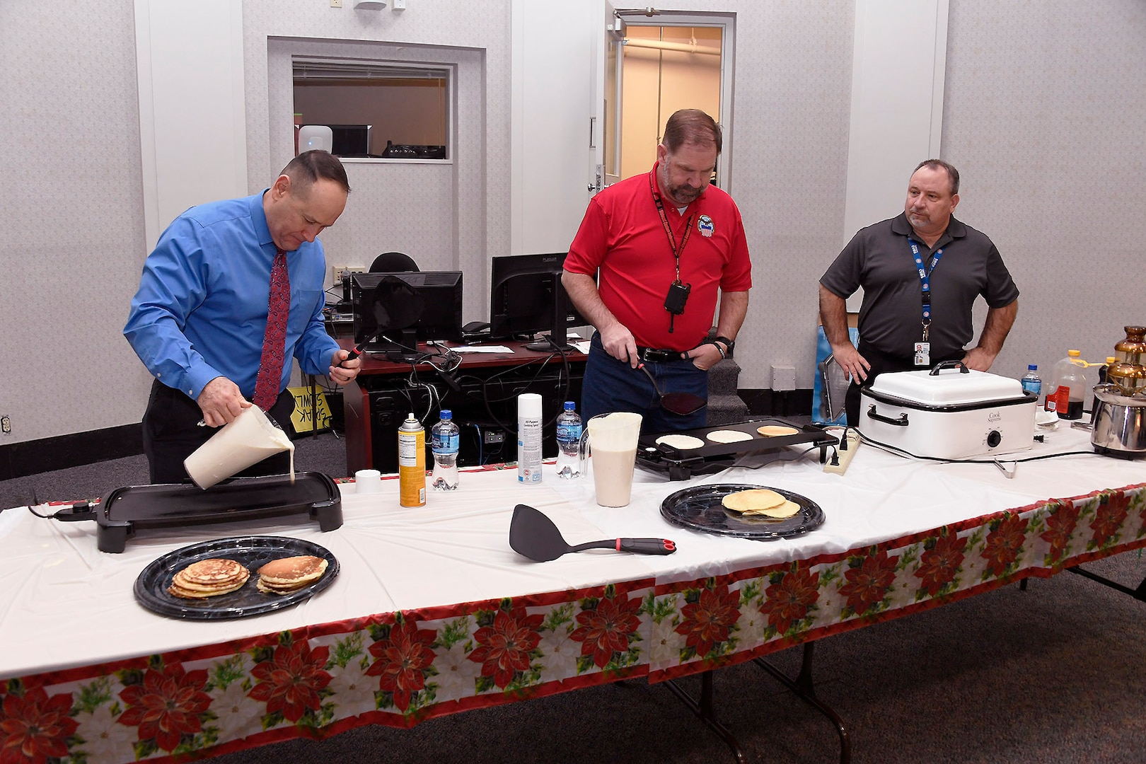 Operations Director Arthur Welsh (far right) watches as DLA Disposition Services Director Mike Cannon (center) and Chief of Staff Peter Foreman grill pancakes for the employees.