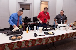 Operations Director Arthur Welsh (far right) watches as DLA Disposition Services Director Mike Cannon (center) and Chief of Staff Peter Foreman grill pancakes for the employees.
