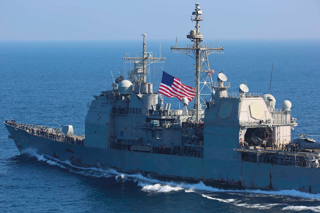 A ship traveling through waters with an American flag flying above.